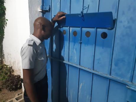Photo by Corey Robinson 
A policeman looks through the peep hole at the Allman Town Police Station in Kingston in response to a knock on the locked gate two weeks ago.