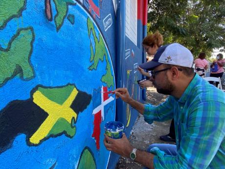 Daniel Beltré (foreground), head of commercial, economic and cultural affairs, Jamaica Embassy of the Dominican Republic and Judith Villar, cultural intern at the embassy, making final touches to a mural they painted hours before the start of the new acad