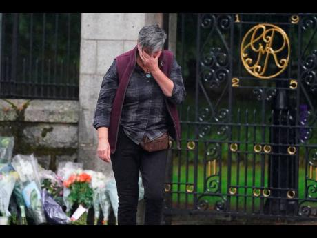 A woman appears emotional after laying flowers at the gates of Balmoral in Scotland following the death of Queen Elizabeth II, on Friday, September 9. 