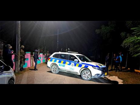 Police gather near the crime scene in Spring Village, Old Harbour, where three persons were killed and six others injured in a gun attack Sunday.