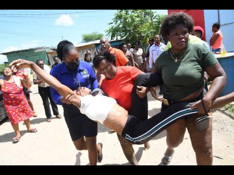 A policewoman (left) assists a woman identified only as Claudia, a cousin of the slain Sasha-Gaye Ebanks, after she fainted in Spring Village on Monday. Claudia was taken to hospital.