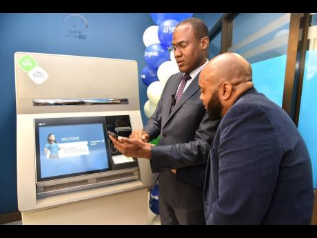 Minister of Finance and the Public Service Dr Nigel Clarke gets instructions from Lynk CEO Vernon James on how to use the Lynk ABM during a launch at the NCB Atrium on Trafalgar Road, St Andrew, on Tuesday.