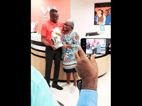 Sean Taylor, branch manager at VMBS Falmouth, presents a gift to  Rhona Anderson (right), the first client to be served at the new VMBS location at Champion Plaza.