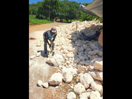 Donald McLean using a sledgehammer to break rocks near Big Pond in St Catherine on Friday as workmen constructed a retaining wall to address a long-standing flooding problem.