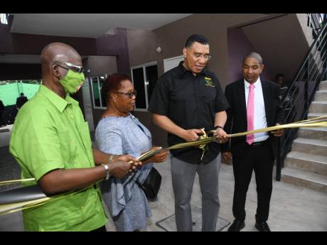 Prime Minister Andrew Holness (second right) cutting the ribbon to mark the official handover of houses to residents on Fourth Street in Bell Rock in his St Andrew West Central constituency on Friday with (from left) Desmond McKenzie, minister of local gov