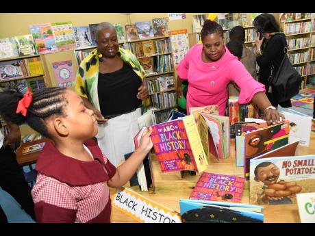 Suelyn Ward-Brown (right), Principal of Jamaica China Goodwill Infant School, Elaine Dickson (second left) of Reading Owls International and student Alafia Polloch examine the books in the just-opened Reading Owls International Library at the Olympic Way-b