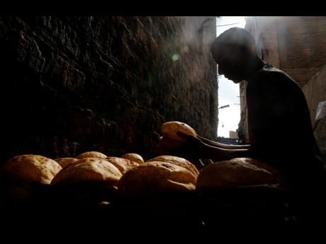 A baker stacks loaves of Egyptian traditional “baladi” flatbread outside a bakery, in the Old Cairo district of Cairo. For decades, millions of Egyptians have depended on the government to keep basic goods affordable. But a series of shocks to the glob