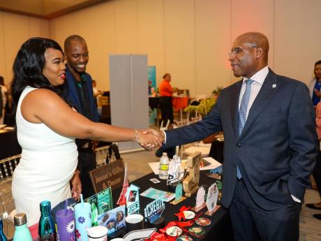 Jerome Cowans (centre) looks on with pride as his wife entrepreneur Kiddist Cowans, CEO of Jesse’s Gifts and Decor, greets Senator Aubyn Hill, the de facto investment minister, at the 2022 Scotiabank Vision Achiever closing ceremony and mini expo at the 