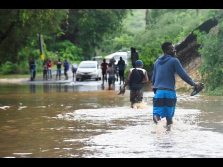 Pedestrians navigate a section of Rasta Corner in Free Town, Clarendon, that was flooded with water from a small gully perpendicular to the road Monday. Vehicle operators were hesitant to drive through the floodwaters.