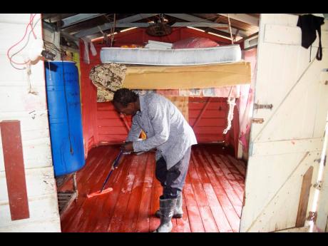 Mattress and sponge hoisted in the ceiling, Dwight Burgess cleans debris from his house Tuesday following day-earlier flooding caused by Hurricane Ian in Halse Hall, Clarendon.