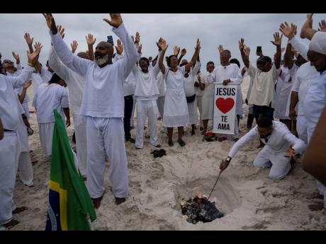 (
Bishop Wedson Tavares, left, leads his flock in prayer asking God to influence the upcoming election as a congregant burns scrawled prayers on scraps of paper in an area of the Abaete dune system, at a steep rise of sand evangelicals call the “Holy Mou