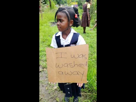 A young student holds a placard as part of a protest staged by residents demanding a bridge in Frankfield, Clarendon.