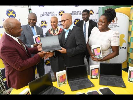 Andrew Lee (third right), chief executive officer of e-Learning Jamaica, presents a laptop to retired Lt Col Gary Rowe (left), commissioner of corrections, during a ceremonial handover of 63 laptops or desktops and 120 tablets to juvenile institutions with
