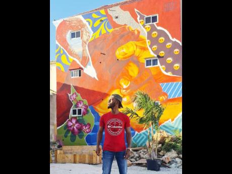 Visual artist and muralist Anthony “Taoszen” Smith posing in front of his work, ‘Connection’ painted at the Kaya Kaya Festival in Otrobanda, Curaçao in August.