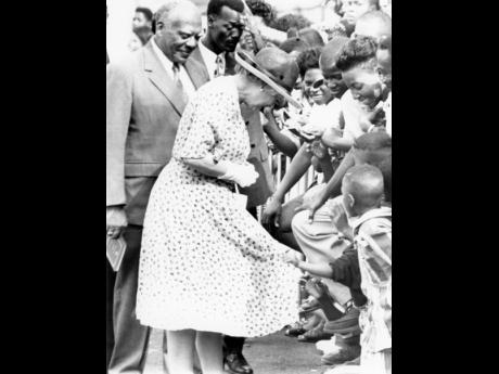 In this March 1, 1994, photograph taken by Rudolph Brown, The Queen falls into the clutches of a child after a tour of the Laws Street Trade Training Centre in central Kingston. The unidentified youngster grabbed briefly at The Queen’s dress to the amuse