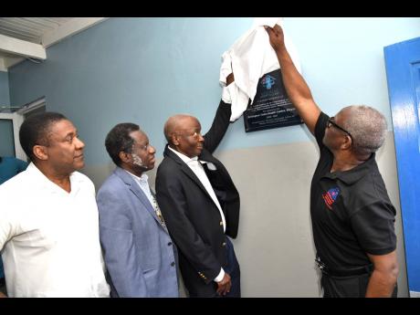 Wentworth Charles (right), chairman of the South East Regional Health Authority, joins Dr Frank Denbow in unveiling the plaque marking the adoption of the Rollington Town Health Centre in Kingston on Friday in a $6-million five-year partnership. Looking on