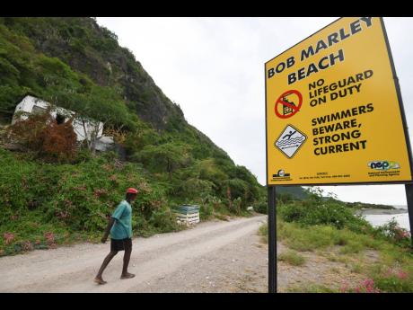 A man walks by a sign at the entrance to Bob Marley Beach in Bull Bay, St Thomas.