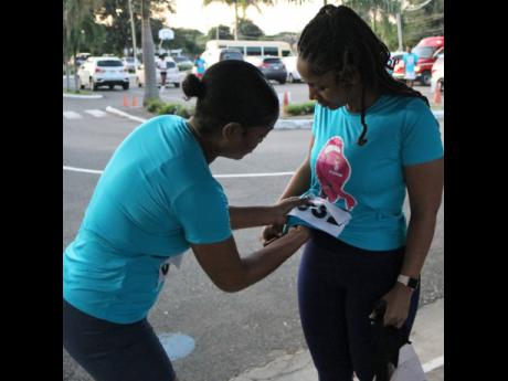Nadia McDonald of the Ministry of Agriculture and Fisheries’ Plant Quarantine Division assists Halle Salmon of the Jamaica Energy Partners Group with her bib ahead of the company’s inaugural Rayz for Life 5K Run last Saturday. 