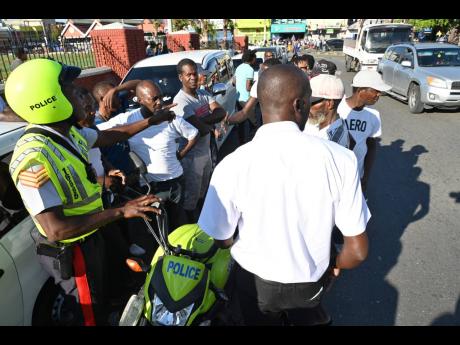 A policeman speaks with taxi operators as they gathered at North Parade in downtown Kingston to strike for a traffic ticket amnesty on Monday, November 14.