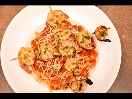 Shrimp arrabbiata: grilled shrimp skewers, brushed with a savoury garlic and herb sauce and served over fettuccine, with sautéed tomatoes and black olives, in a spicy garlic tomato sauce and finished with Parmesan cheese.