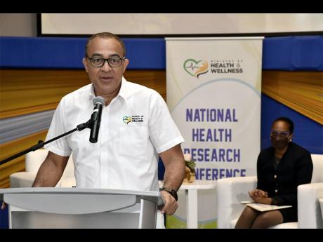 Dr Christopher Tufton, minister of health and wellness, speaking at the National Health Research Conference on Wednesday at AC Hotel in Kingston. In the background is Dr Karen Webster-Kerr, national epidemiologist. 