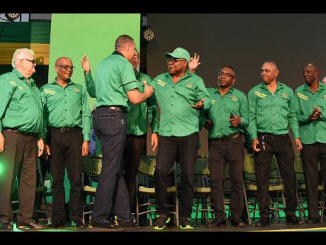Demoted State Minister J.C. Hutchinson (right) awaits his turn to be greeted by Jamaica Labour Party leader Andrew Holness at the party's 79th annual conference on Sunday.