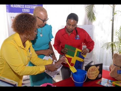 Minister of Education and Youth Fayval Williams (centre) looks on as executive director of the Early Childhood Commission (ECC), Karlene DeGrasse-Deslandes (left), shows her some of the resources used to engage students. Looking on is ECC Chair Trisha Will
