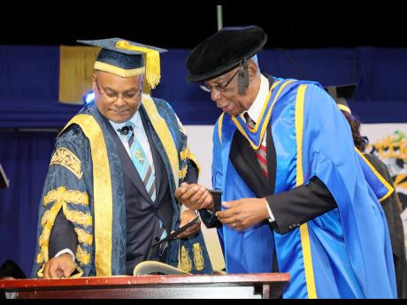 Engineer Alfrico Adams (right) prepares to sign the register of honorary graduates following his conferment of the Doctor of Technology, Honoris Causa by UTech, Jamaica Chancellor Lloyd Carney (left) at the ceremony for the Presentation of Graduates Class 