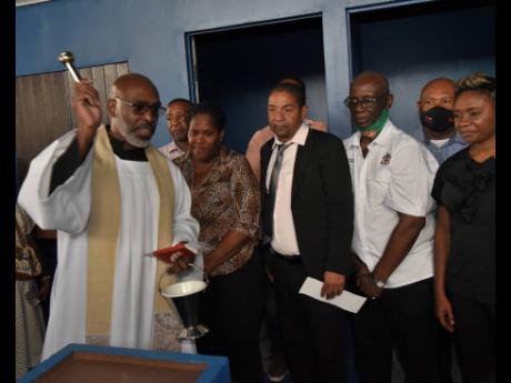 Reverend Khan Honeyghan (left) of the St Jude’s Anglican Church in Stony Hill, St Andrew, blessing the Stony Hill Market during the official re-opening ceremony.  Looking on are from (second left) Councillor Andrew Swaby from the Vineyard Town Division; 
