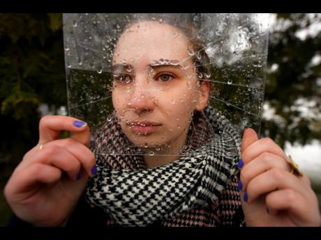 A woman poses holding a piece of cracked plastic sheet during a flash mob to raise awareness of the increased levels of violence against women since the COVID-19 pandemic, in Bucharest, Romania, on March 10, 2021. 