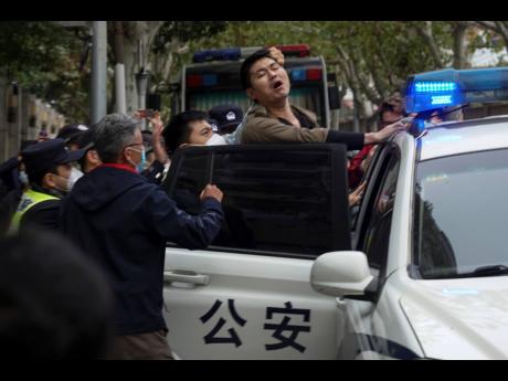 In this photo taken on Sunday, November 27, a protester reacts as he is arrested by policemen during a protest on a street in Shanghai, China.