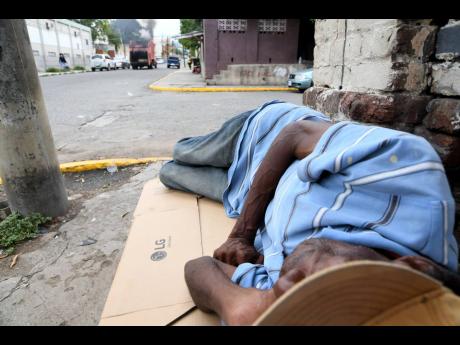 A homeless man uses a flattened cardboard box as a bed to sleep on a sidewalk in downtown Kingston. 