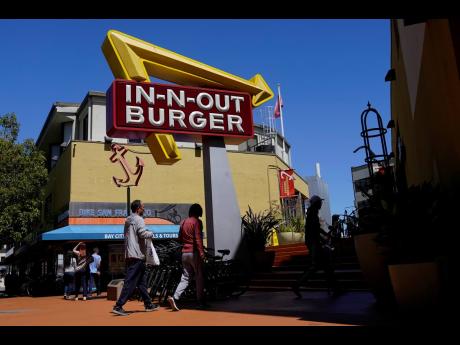 People walk below an In-N-Out Burger restaurant sign in San Francisco, August 25, 2022. The nation’s employers kept hiring briskly in November despite high inflation and a slow-growing economy.