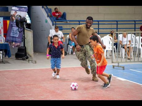 Hospital Corpsman 3rd Class Lou-Shane Daley, from Linstead, St Catherine, play football with kids at a medical site set up in the Sports Coliseum of Combat and Gymnastics in Cartagena, Colombia, on November 15. Comfort is deployed to US 4th Fleet in suppor