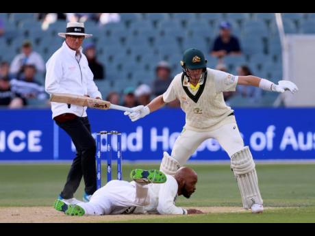 West Indies' Roston Chase (bottom) dives on the ground while fielding as Australia's batsman Marnus Labuschagne (right) looks on during the opening day of the second Test match in Adelaide, Thursday, November 8, 2022. 