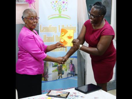 Caught off guard by a surprise tribute in her honour, outgoing principal of the Gospel Refuge Tabernacle  Basic School accepts a token of appreciation from a representative of the Canada-based charity Lend a Helping Hand at the school, located in the Stand