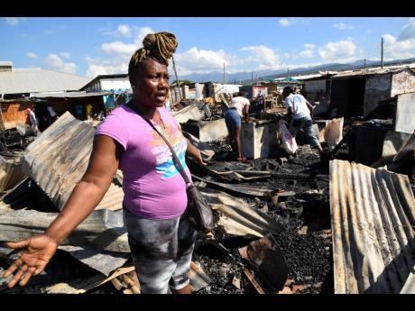 Sherryl Williams, whose wares were spared by Sunday’s fire in downtown Kingston, talks to journalists amid the razed rubble. 