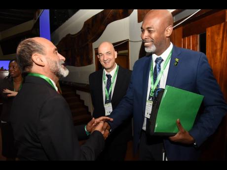 Ainsley Henry (right), CEO and conservator of forests at the Forestry Department, greets Dr Crispim Moreira (left), FAO representative to Jamaica, during the National Forestry Conference  at the Jamaica Conference in Kingston on December 7. Looking on is A