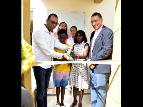 From left, foreground: Norman Horne, chairman for ARC Properties Limited, assists 14-year-old Rohan Clarke and his mother, Sidonie Eldermire, to cut the ribbon to their new home in Olympic Gardens, St Andrew, on Thursday as Prime Minister Andrew Holness lo