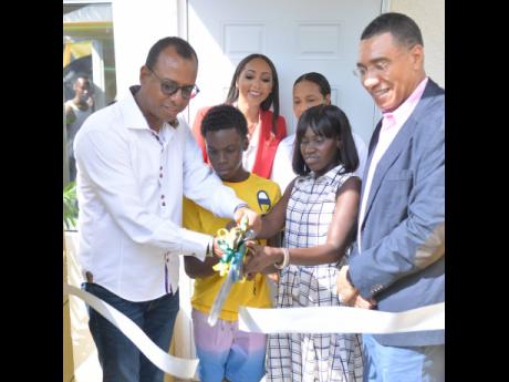 Prime Minister Andrew Holness (right), looks on as beneficiary Sidonie Eldemire (second right), her son Rohan Clarke (second left) and Chairman, Arc Properties Limited, Norman Horne, cut the ribbon during a handover ceremony for a two-bedroom house that sh