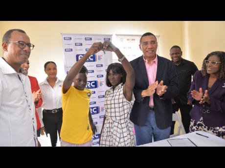 Prime Minister Andrew Holness (third right), applauds as new beneficiary, Sidonie Eldemire (fourth right), and son Rohan Clarke (fourth left), display the keys to their home, which they received under the New Social Housing Programme. The unit was construc