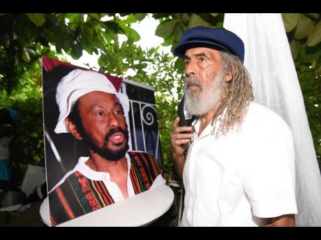 Allan ‘Skill’ Cole, stands next to a picture of Dr Carlton ‘Pee Wee’ Fraser, former Reggae Boyz doctor.