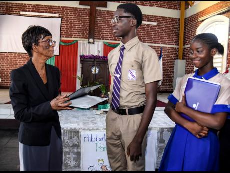 From left: Valerie Hibbert hands over a laptop to Anando Richards, fifth form Kingston College student, as Marshilena McDonald, second form student of Holy Childhood High School looks on. Hibbert handed laptops at a parenting workshop at Jones Town Baptist