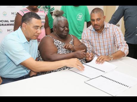 Prime Minister Andrew Holness (left) and Mikael Phillips, member of parliament for Manchester North Western, assist Violet Johnson of Comfort Hall in signing a contract after receiving a free three-bedroom home under the New Social Housing Project on Frida