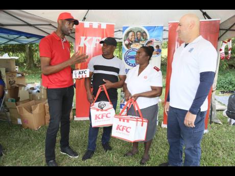 Andrei Roper (left), brand manager of Restaurants of Jamaica, operator of KFC, hands over 1,300 meal vouchers to Food for the Poor Angels of Hope Christmas Outreach Jamaica last Friday. Sharing in the moment are (from second left) Richard McLean, health an