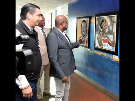 Edmund Bartlett (right), minister of tourism; Fernando Vistrain (left), CEO, PAC Kingston Airport Limited; and Dr Carey Wallace, executive director, Tourist Enhancement Fund, look at pictures of West Indies Cricketer Christopher Gayle and Olympian Shelly-A