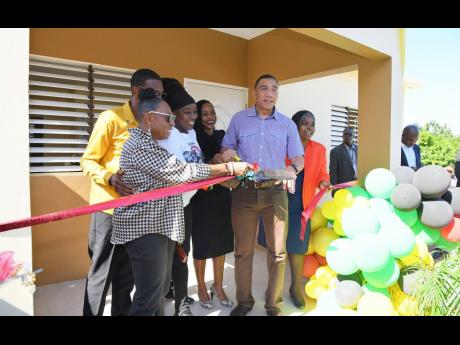Prime Minister Andrew Holness (fifth left) cuts the ribbon to officially hand over a two-bedroom unit in Seville Heights, St Ann, to New Social Housing Programme beneficiary Jacinth Johnson (third left), on Monday, December 19. Also sharing the moment (fro