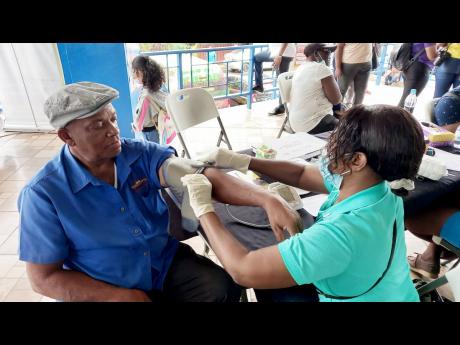 Community health aide, Sharlene Carty administers blood sugar and blood pressure tests for taxi operator Ruddy Wint at the 1000 Man Strong health fair held on the grounds of the May Pen Police Station on Tuesday, December 20.