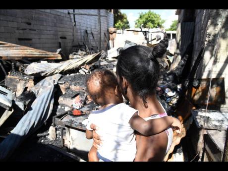 Tyshie Williams holds one of her four children in her arms as she surveys the charred rubble where her home once stood on Cleveland Road in Kingston on Friday. It was one of two homes razed in an alleged firebombing attack Thursday afternoon.