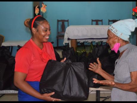 Celine Daley, accounts payable clerk at the Shipping Association of Jamaica, presents a care package to one of 50 elderly residents who benefited from the body’s annual treat.